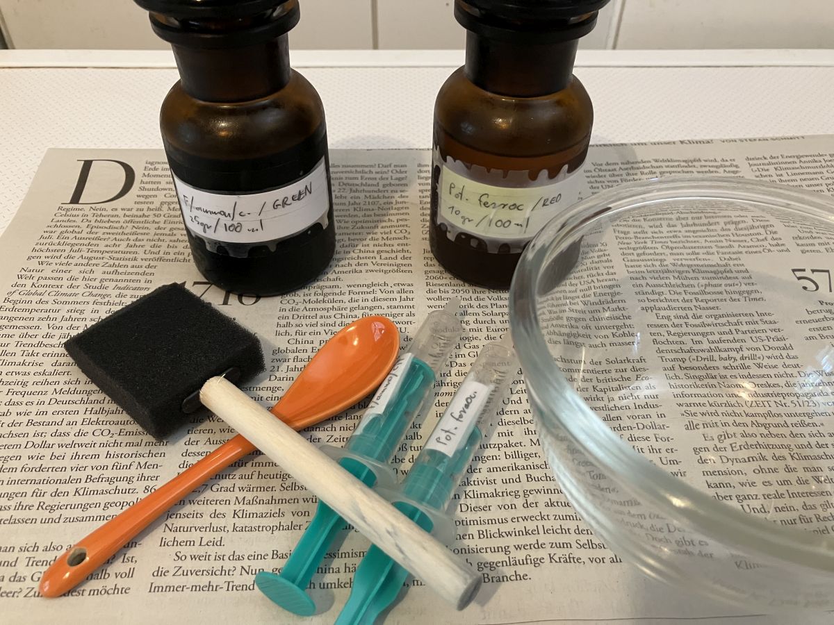 Two small, hand-labeled brown glass bottles. Two plastic syringes, a plastic brush, a ceramic spoon and a glass bowl are at the front.